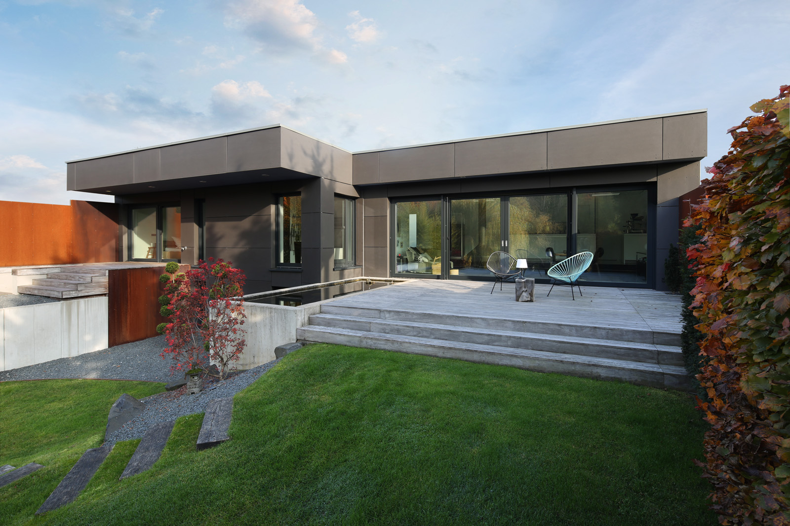 Haus am See – Gartenfassade des Flachdach-Bungalows mit Terrasse und Cortenstahl-Wänden