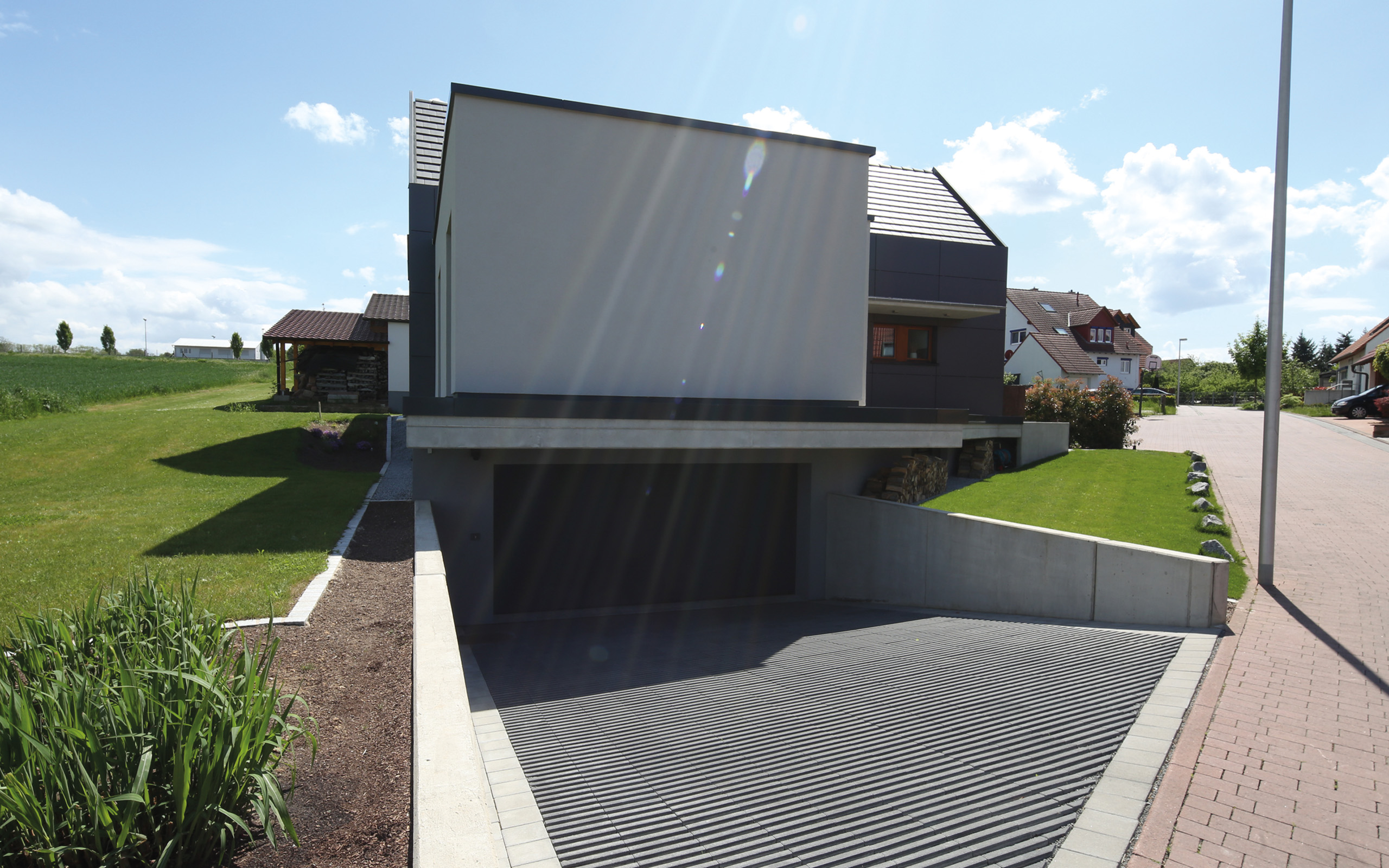 Aus- und Einblick – Straßenansicht mit dunkler Garagenzufahrt und auskragendem Obergeschoss