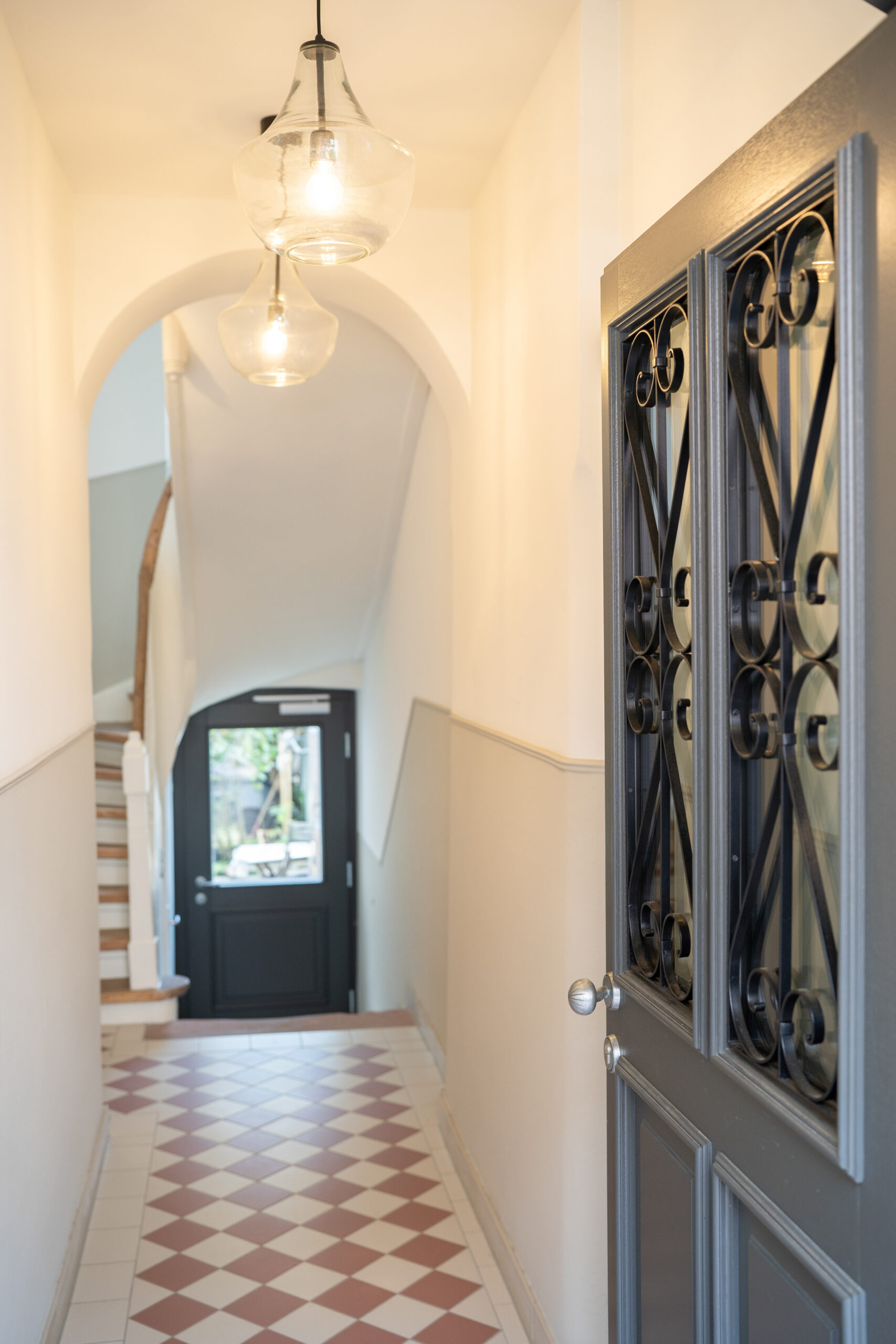 Saniertes Gründerzeit-Treppenhaus – Flur mit Glas-Pendelleuchten und schmiedeeiserner Glastür