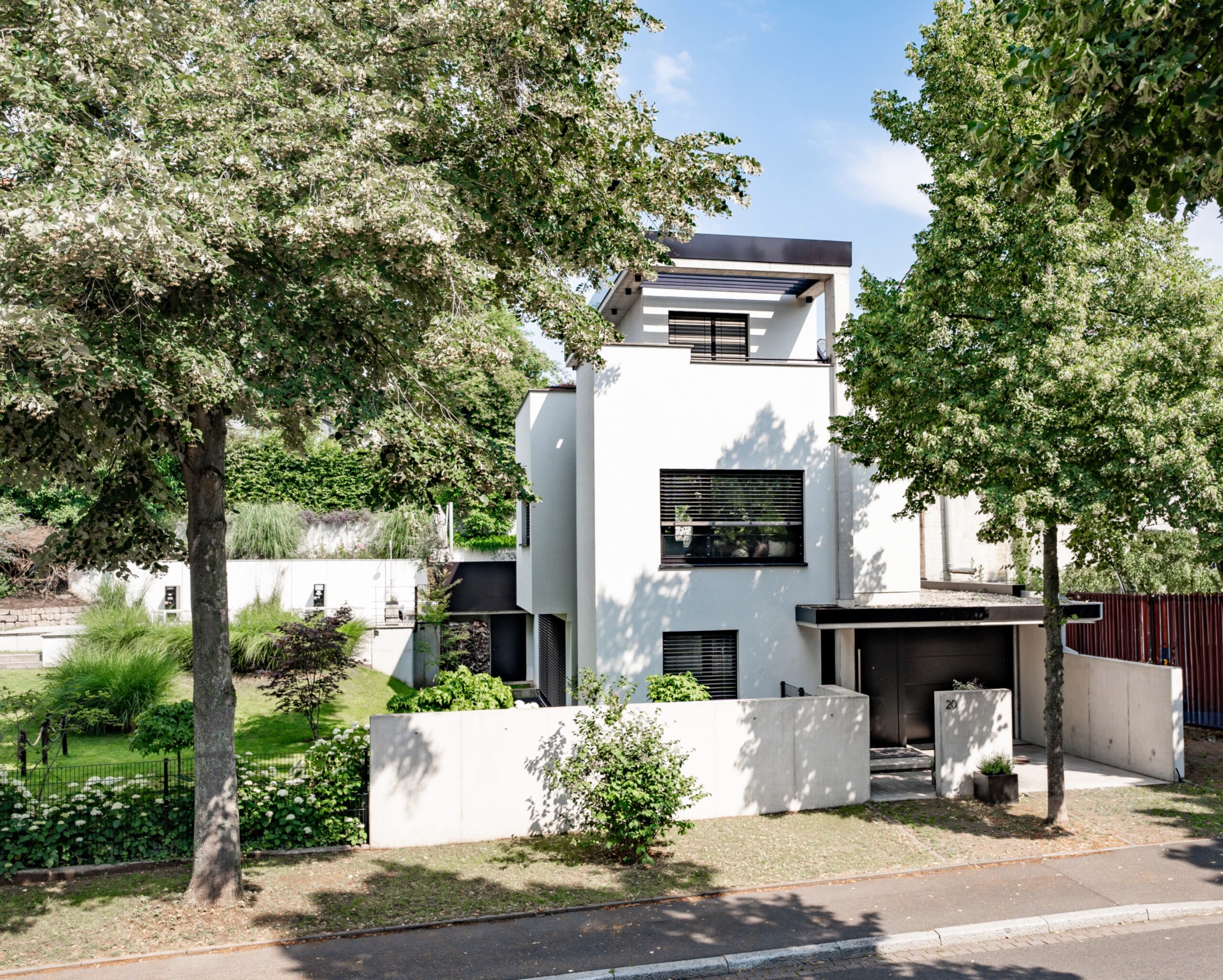 Haus WIE – Straßenansicht des dreigeschossigen weißen Wohnhauses unter Bäumen