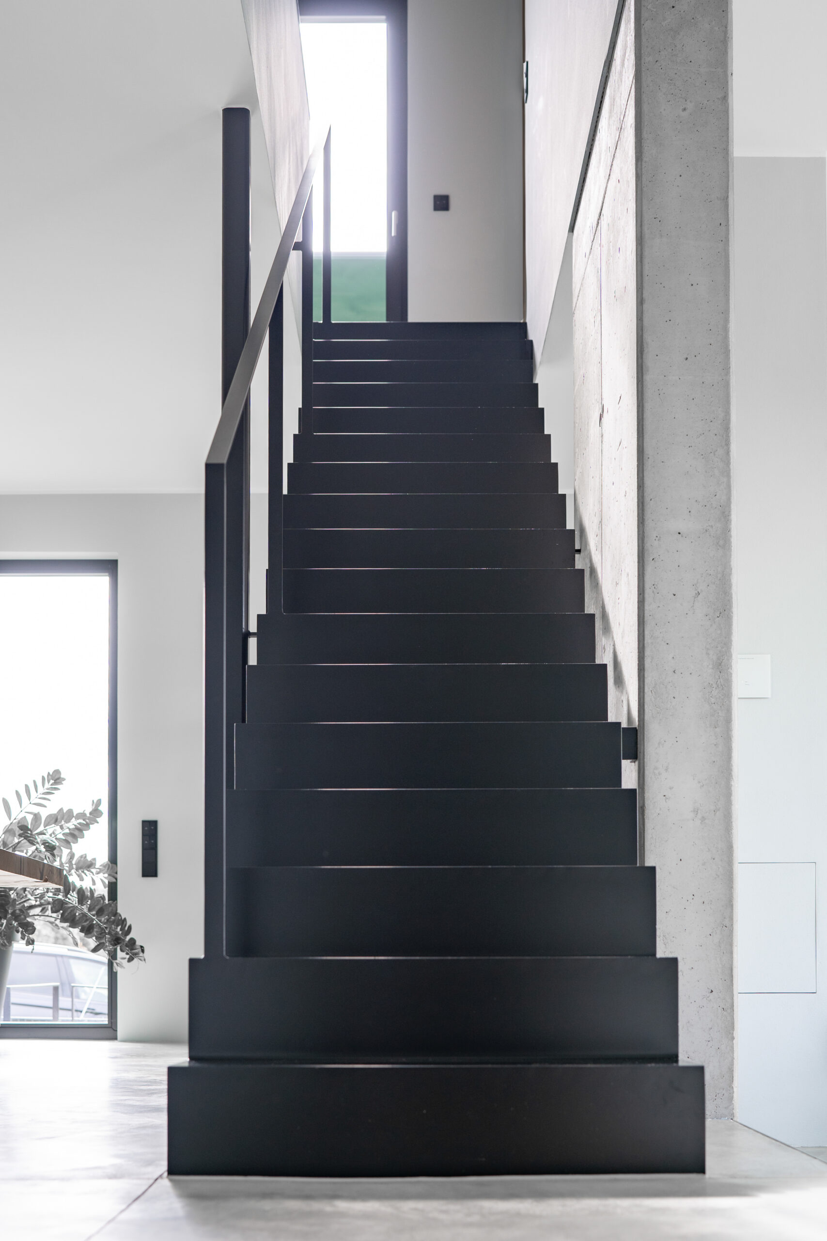 Haus LGW – schwarze Faltwerktreppe aus Stahl vor Sichtbetonwand