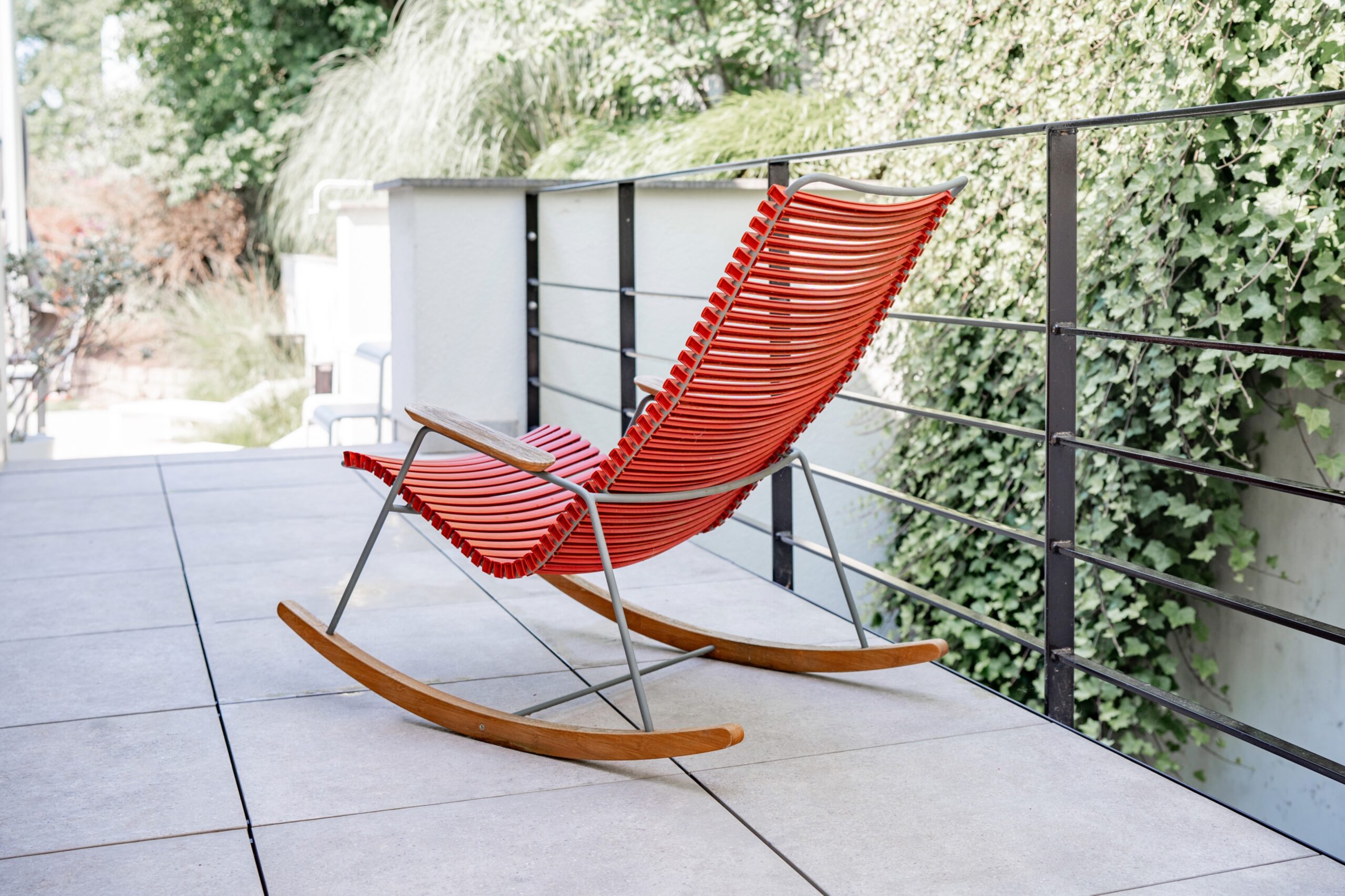 Haus WIE – roter Design-Schaukelstuhl auf der Terrasse mit filigranem Stahlgeländer
