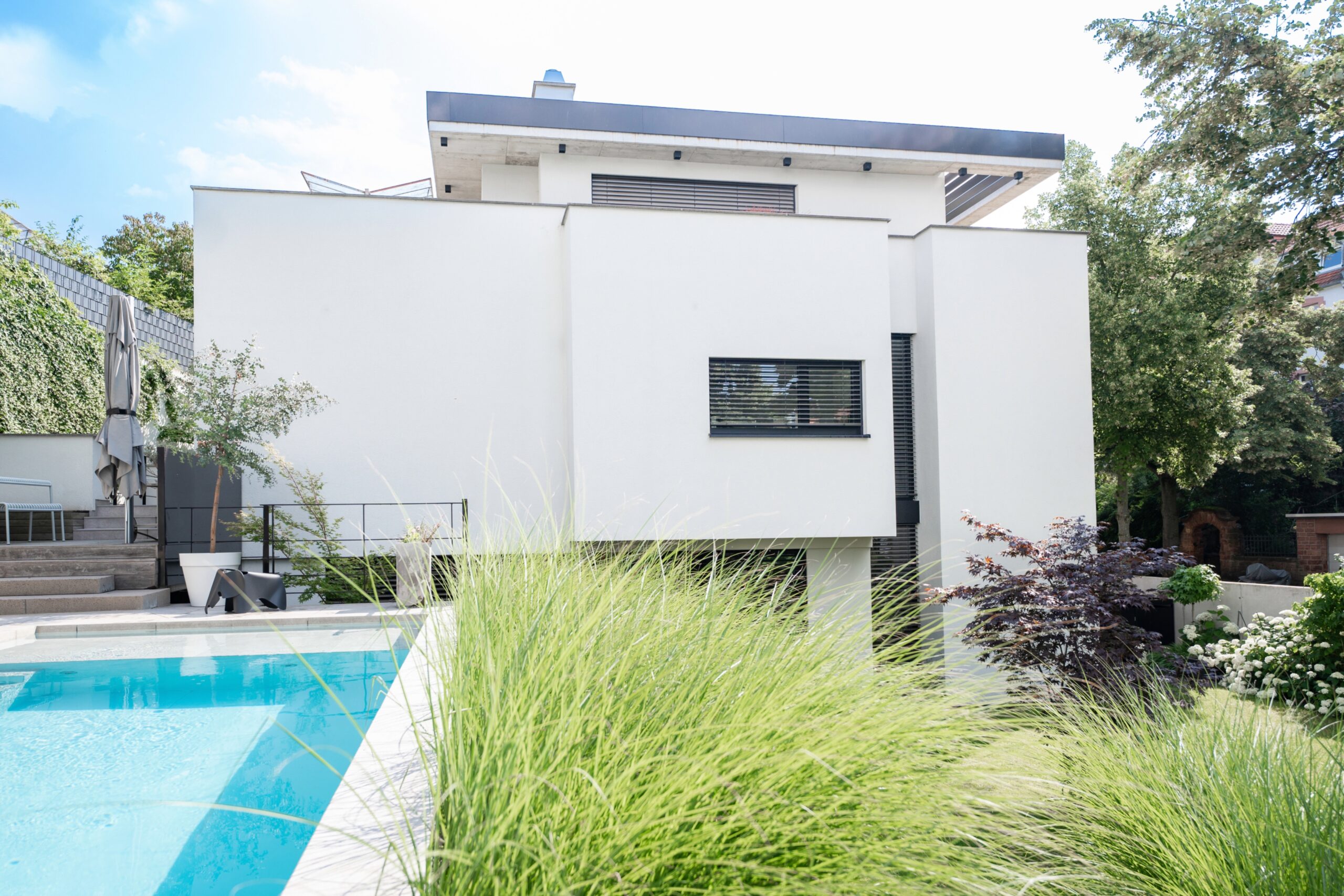 Haus WIE – Blick über den Pool auf die weiße Gartenfassade