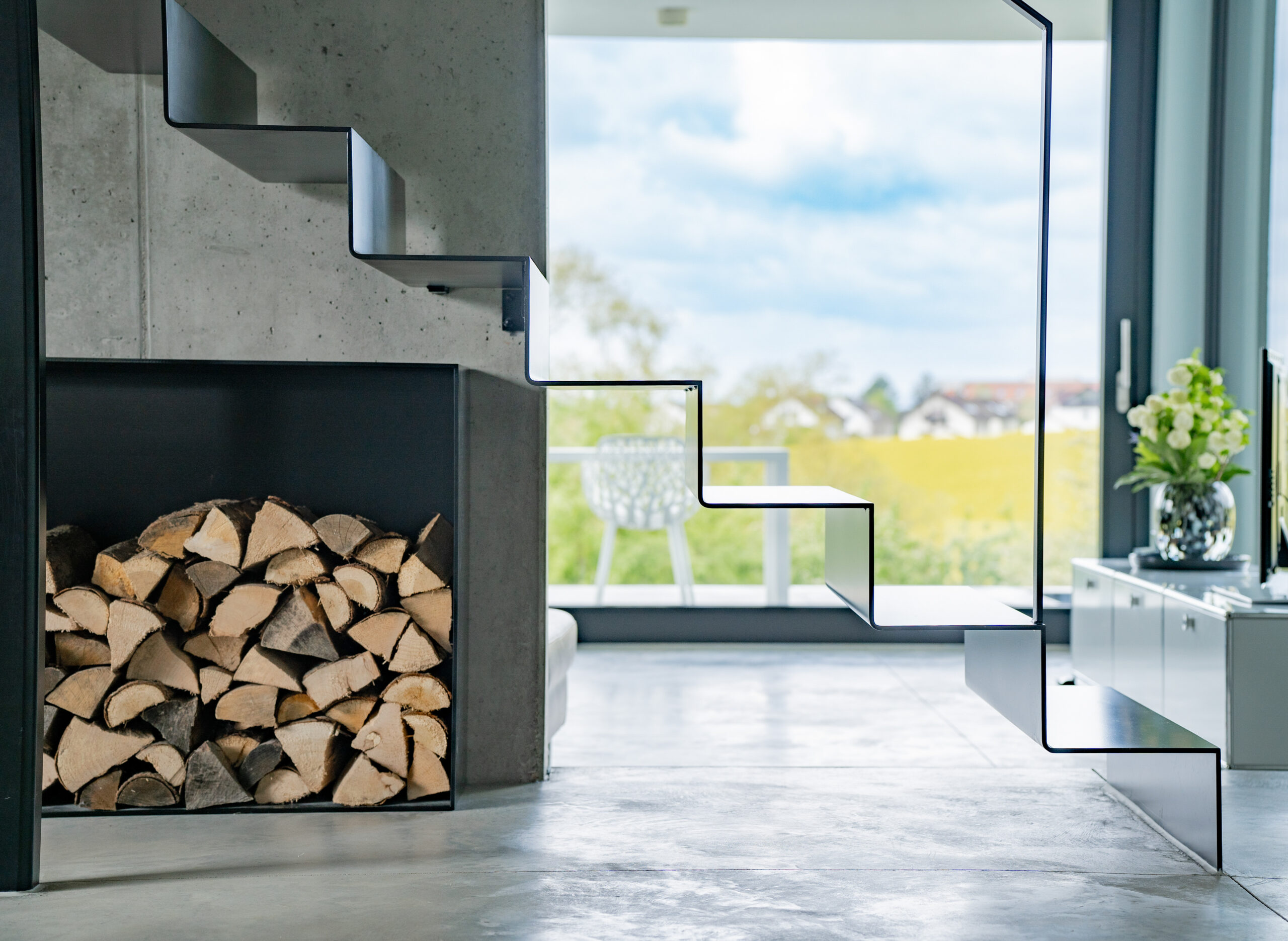 Haus LGW – Kamin mit Brennholzfach unter der Treppe, Sichtbeton und Panoramafenster